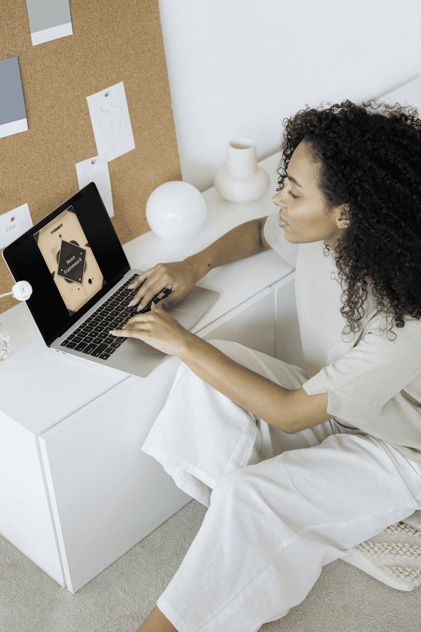 Woman sitting on a white couch using a laptop with a minimalistic background